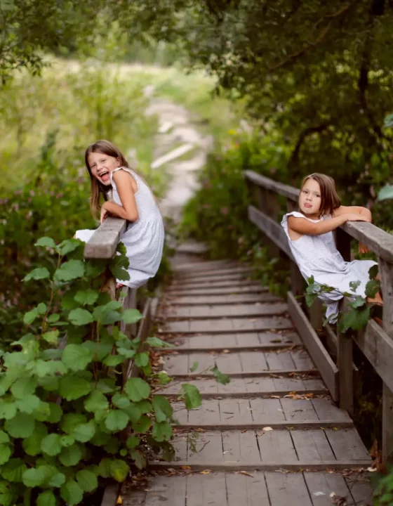 Children siblings play climb on a wooden bridge in summer, childhood emotions, summer walks with children in the village. A wooden bridge and children hang on the railing.