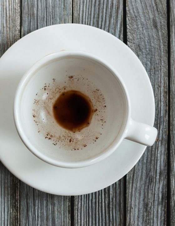 Empty cup with coffee leftovers on wooden table, closeup